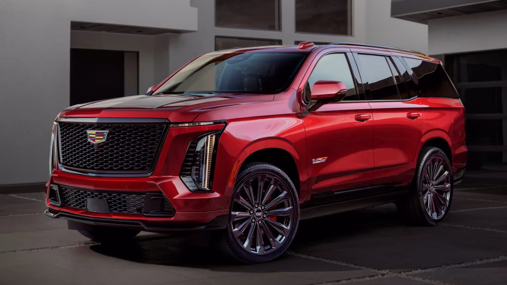 2025-cadillac-escalade-v-101-69a08520156d8 | Wagner Certified Collision Red luxury SUV shown from a front-right perspective, highlighting a large black mesh grille and bold chrome accents beside a modern building backdrop.