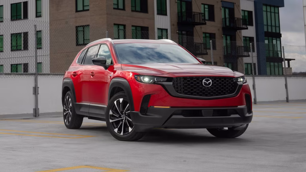 Front-left three-quarter view of a red Mazda SUV parked on a rooftop parking lot with city buildings in the background.