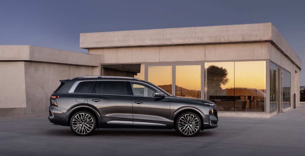 Grey SUV parked in front of a modern concrete building with glass walls at sunset.