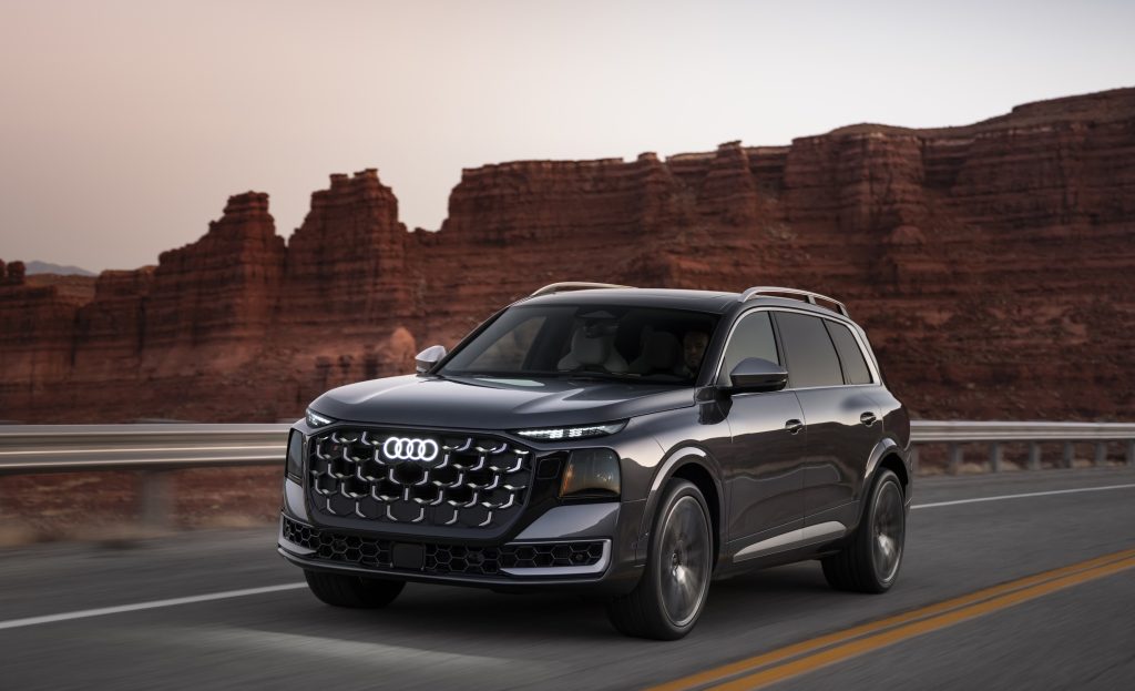 Dark gray Audi SUV driving on a highway with red rock canyon walls in the background at dusk/sunset.