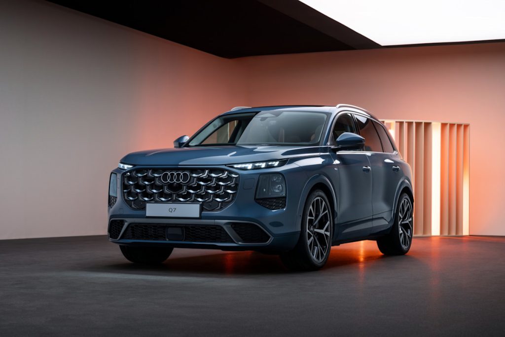 Front three-quarter view of a blue Audi Q7 SUV on a showroom floor with warm wall lighting and a bold grille.