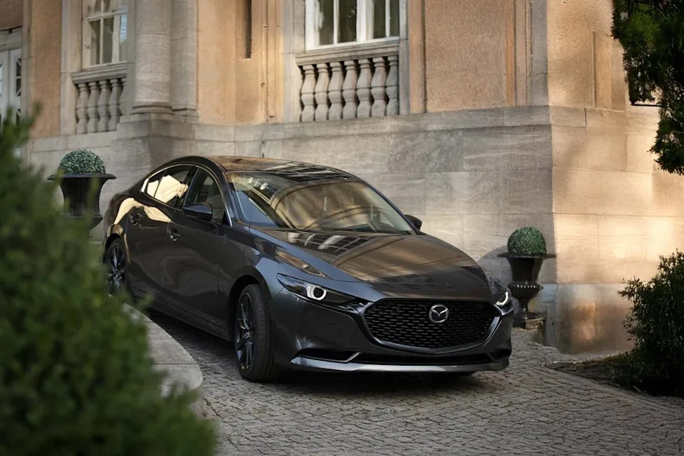 Dark gray Mazda sedan parked on a stone driveway in front of an ornate stone building with columns and balustrades.