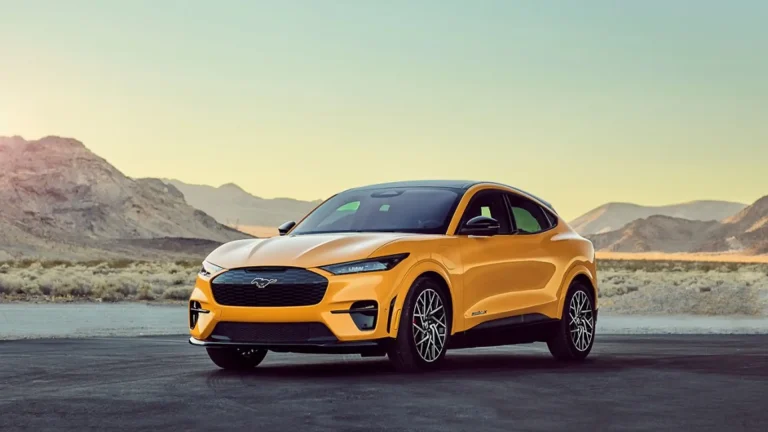 Yellow Ford Mustang Mach-E electric SUV on a desert road with rocky hills at sunset.
