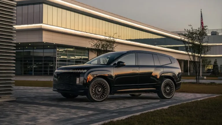 Black luxury SUV parked in front of a modern showroom at dusk with an American flag nearby