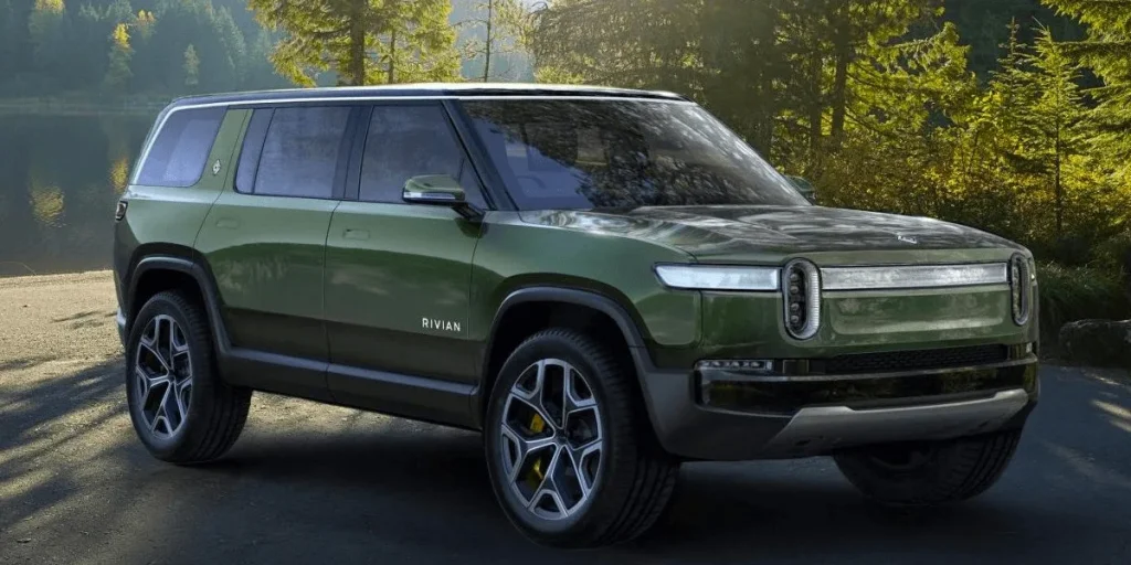 rivian-automotive-r1s-concept-car-2018-03-1png | Wagner Certified Collision Green Rivian SUV parked on a forest road by a lake, with trees in the background and yellow brake calipers visible through the wheels.