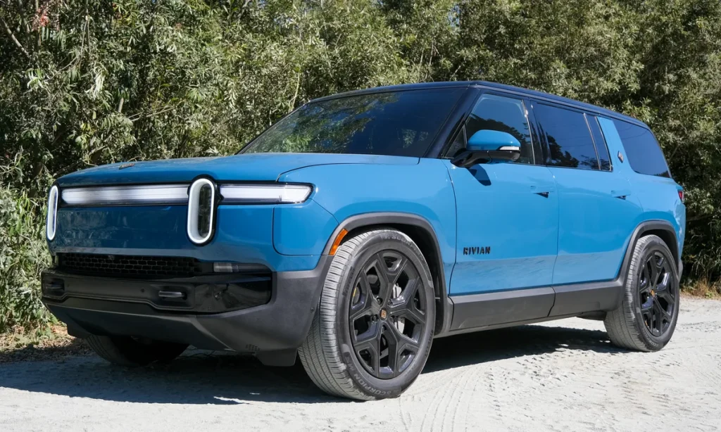 rivian-r1s | Wagner Certified Collision Blue Rivian R1S SUV parked on a dirt road with trees in the background on a sunny day.