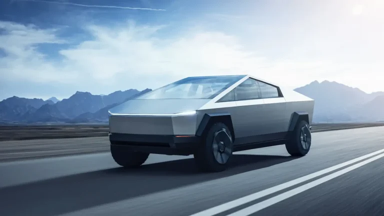 Sleek, silver futuristic electric car driving on a highway with blue sky and distant mountains in the background.