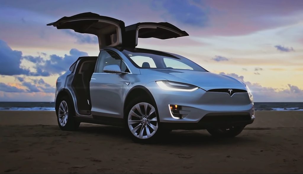 tesla-model-x-1 | Wagner Certified Collision Tesla Model X with gull-wing doors raised, parked on a sandy beach at sunset.
