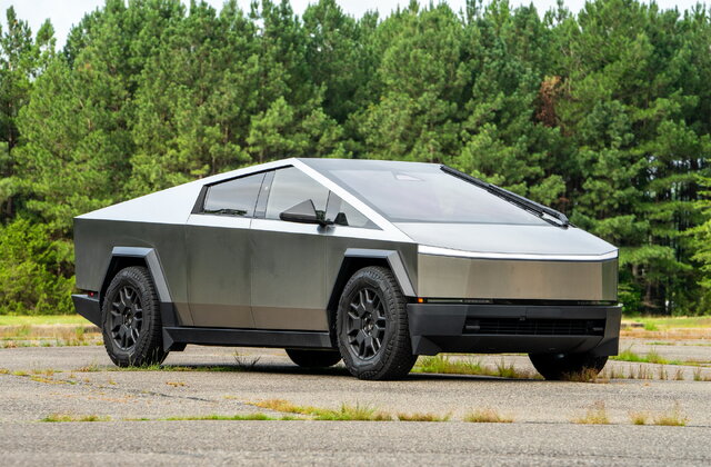 usnpx-2024teslacybertruck-angularfront-zd | Wagner Certified Collision Futuristic, angular gray and silver electric car parked on a paved lot with a forested background.